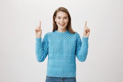 Imponująca szczęśliwa caucasian blondynki kobieta wskazuje up, jest ubranym błękitnego pulower, ono uśmiecha się szeroko i wyraża Zdjęcie Royalty Free Imponująca szczęśliwa caucasian blondynki kobieta wskazuje up, jest ubranym błękitnego pulower, ono uśmiecha się szeroko i wyraża Zdjęcie Royalty Free