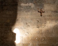 Incrocio di legno che appende su una vecchia parete di pietra in una chiesa, parzialmente accesa con i raggi del sole immagine stock Incrocio di legno che appende su una vecchia parete di pietra in una chiesa, parzialmente accesa con i raggi del sole immagine stock
