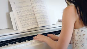 Indietro della giovane donna che gioca il piano nella stanza luminosa, tenuto in mano Indietro della giovane donna che gioca il piano nella stanza luminosa, tenuto in mano
