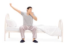 Individuo joven que se sienta en una cama y que bosteza fotos de archivo libres de regalías Individuo joven que se sienta en una cama y que bosteza fotos de archivo libres de regalías