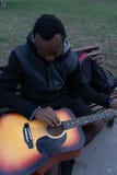 Indivíduo africano com uma guitarra acústica em uma mala de viagem que prepara-se para jogar no parque foto de stock Indivíduo africano com uma guitarra acústica em uma mala de viagem que prepara-se para jogar no parque foto de stock