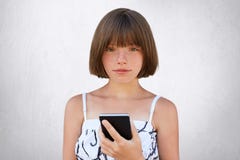 Infanzia nell'era digitale Ragazza sveglia con la breve pettinatura alla moda, gli occhi incavati scuri e le lentiggini portanti immagine stock Infanzia nell'era digitale Ragazza sveglia con la breve pettinatura alla moda, gli occhi incavati scuri e le lentiggini portanti immagine stock