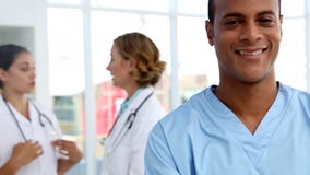 Infirmière souriant et se tenant devant l'équipe médicale banque de vidéos Infirmière souriant et se tenant devant l'équipe médicale banque de vidéos