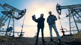 Ingegneri che stanno su un giacimento di petrolio su un fondo del sole, vista dal basso video d archivio Ingegneri che stanno su un giacimento di petrolio su un fondo del sole, vista dal basso video d archivio