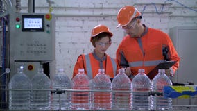 Ingénieurs type et fille dans le casque et vêtements de fonctionnement près de ligne de convoyeur pour mettre l'eau en bouteille banque de vidéos Ingénieurs type et fille dans le casque et vêtements de fonctionnement près de ligne de convoyeur pour mettre l'eau en bouteille banque de vidéos