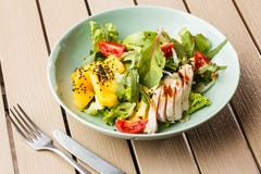 Insalata con il pollo arrostito, mango, lattuga, avocado, pomodori, rucola, sause del formaggio su un piatto bianco su di legno fotografia stock libera da diritti Insalata con il pollo arrostito, mango, lattuga, avocado, pomodori, rucola, sause del formaggio su un piatto bianco su di legno fotografia stock libera da diritti