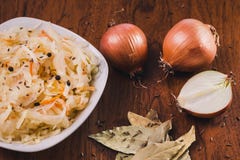 Insalata dei crauti e carote con pepe nero in un piatto bianco ed alcuni cipolle, foglie dell'alloro e semi di cumino fotografia stock libera da diritti Insalata dei crauti e carote con pepe nero in un piatto bianco ed alcuni cipolle, foglie dell'alloro e semi di cumino fotografia stock libera da diritti