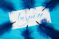Inspire. Beautiful blue letters on canvas in feathers frame. Calligraphy script. Art of writing letters. Background stock image Inspire. Beautiful blue letters on canvas in feathers frame. Calligraphy script. Art of writing letters. Background stock image