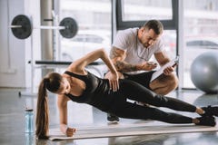 Instructor personal masculino que mira el contador de tiempo y a la mujer atlética joven imagen de archivo libre de regalías Instructor personal masculino que mira el contador de tiempo y a la mujer atlética joven imagen de archivo libre de regalías