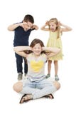 Irmã idosa irritada Adolescente que cobre suas orelhas com seus mãos, irmão novo e irmã gritando em suas orelhas imagens de stock Irmã idosa irritada Adolescente que cobre suas orelhas com seus mãos, irmão novo e irmã gritando em suas orelhas imagens de stock