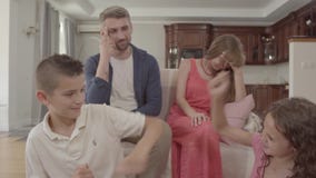 Irmão e irmã que discutem no primeiro plano, na mãe confusa e no pai sentando-se no sofá no fundo navega??o filme Irmão e irmã que discutem no primeiro plano, na mãe confusa e no pai sentando-se no sofá no fundo navega??o filme