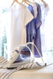 Iron on ironing board with clothes hanging