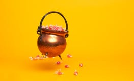 Iron pot with multi-colored sweets on blank orange background.