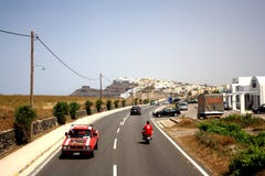 Isola di Santorini, Grecia - 5 maggio 2013: Una strada sull'isola con un'automobile rossa e un uomo sul motocycle immagini stock Isola di Santorini, Grecia - 5 maggio 2013: Una strada sull'isola con un'automobile rossa e un uomo sul motocycle immagini stock