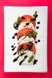 Italiaanse Caprese-salade met de Oregozwarte peper van de Mozarellatomaat en Balsemieke Azijn op Witte Plaat op Rode Achtergrond Royalty-vrije Stock Fotografie Italiaanse Caprese-salade met de Oregozwarte peper van de Mozarellatomaat en Balsemieke Azijn op Witte Plaat op Rode Achtergrond Royalty-vrije Stock Fotografie