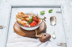 Italiensk tomat-, vitlök- och basilikasoppaPappa al Pomodoro i metallbunke med bröd på lantligt träbräde över ljus - blått arkivbilder Italiensk tomat-, vitlök- och basilikasoppaPappa al Pomodoro i metallbunke med bröd på lantligt träbräde över ljus - blått arkivbilder