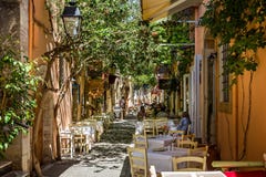 Jantares que sentam-se em cafés exteriores na aleia estreita sob a luz solar dappled na Creta, Grécia imagem de stock Jantares que sentam-se em cafés exteriores na aleia estreita sob a luz solar dappled na Creta, Grécia imagem de stock