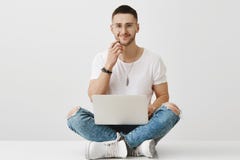 Je m'enregistrerai pour cette concurrence Mâle européen beau enthousiaste s'asseyant sur le plancher avec les jambes croisées images stock Je m'enregistrerai pour cette concurrence Mâle européen beau enthousiaste s'asseyant sur le plancher avec les jambes croisées images stock