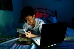Jeune adolescent devant un ordinateur portable et sur un lit et à l'aide d'un comprimé images stock Jeune adolescent devant un ordinateur portable et sur un lit et à l'aide d'un comprimé images stock
