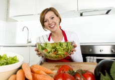Jeune belle femme à la maison de cuisinier à la cuisine moderne préparant le sourire végétal de saladier heureux photo stock Jeune belle femme à la maison de cuisinier à la cuisine moderne préparant le sourire végétal de saladier heureux photo stock