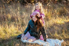 Jeune belle mère avec sa fille sur une promenade un jour ensoleillé d'automne La fille essaye de mettre son chapeau sur la mère, image stock Jeune belle mère avec sa fille sur une promenade un jour ensoleillé d'automne La fille essaye de mettre son chapeau sur la mère, image stock