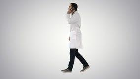 Jeune docteur parlant ? mobile et au walkind sur le fond de gradient photo stock Jeune docteur parlant ? mobile et au walkind sur le fond de gradient photo stock