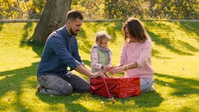 Jeune famille affectueuse essayant de défaire le ruban du cadeau d'anniversaire banque de vidéos Jeune famille affectueuse essayant de défaire le ruban du cadeau d'anniversaire banque de vidéos