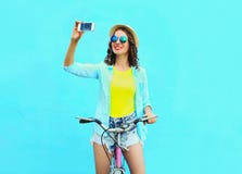 Jeune femme assez fraîche prenant l'autoportrait sur le smartphone avec la rétro bicyclette au-dessus du bleu coloré photos stock Jeune femme assez fraîche prenant l'autoportrait sur le smartphone avec la rétro bicyclette au-dessus du bleu coloré photos stock
