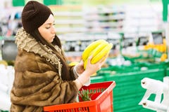 Jeune femme avec le panier à provisions choisissant la banane pendant les achats au supermarché photographie stock Jeune femme avec le panier à provisions choisissant la banane pendant les achats au supermarché photographie stock