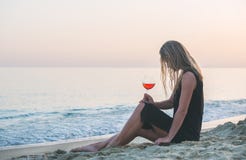 Jeune femme blonde détendant avec le verre de vin rosé sur la plage par la mer au coucher du soleil image libre de droits Jeune femme blonde détendant avec le verre de vin rosé sur la plage par la mer au coucher du soleil image libre de droits