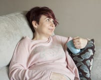 Jeune femme dans la grossesse tôt se reposant sur le divan photographie stock Jeune femme dans la grossesse tôt se reposant sur le divan photographie stock