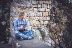 Jeune femme de sourire détendant dehors avec le téléphone portable dans le media social pendant elle le voyage photos stock Jeune femme de sourire détendant dehors avec le téléphone portable dans le media social pendant elle le voyage photos stock