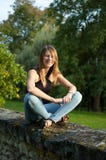 Jeune femme de sourire mignonne s'asseyant en parc pendant le coucher du soleil dans les jeans et la chemise noire et regardant l photos stock Jeune femme de sourire mignonne s'asseyant en parc pendant le coucher du soleil dans les jeans et la chemise noire et regardant l photos stock