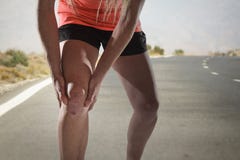 Jeune femme de sport avec les jambes sportives fortes tenant le genou avec des mains dans la blessure de souffrance de ligament d photos stock Jeune femme de sport avec les jambes sportives fortes tenant le genou avec des mains dans la blessure de souffrance de ligament d photos stock