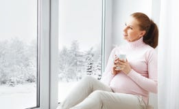 Jeune femme enceinte heureuse avec la tasse de thé sur la fenêtre image libre de droits Jeune femme enceinte heureuse avec la tasse de thé sur la fenêtre image libre de droits