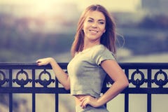 Jeune femme heureuse de mode dans le dessus gris de culture se penchant sur la balustrade photographie stock libre de droits Jeune femme heureuse de mode dans le dessus gris de culture se penchant sur la balustrade photographie stock libre de droits