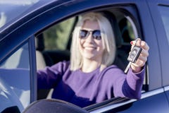 Jeune femme heureuse montrant des clés de sa première vue de côté automobile images stock Jeune femme heureuse montrant des clés de sa première vue de côté automobile images stock