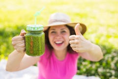 Jeune femme heureuse montrant des pouces avec les smoothies verts à un pique-nique Nourriture, detox et concept sains de régime photo libre de droits Jeune femme heureuse montrant des pouces avec les smoothies verts à un pique-nique Nourriture, detox et concept sains de régime photo libre de droits