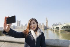 Jeune femme heureuse prenant l'autoportrait par le téléphone portable contre Big Ben à Londres, Angleterre, R-U photographie stock libre de droits Jeune femme heureuse prenant l'autoportrait par le téléphone portable contre Big Ben à Londres, Angleterre, R-U photographie stock libre de droits