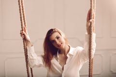 Jeune femme rousse attirante avec de longs cheveux se reposant sur l'oscillation dans la chemise du ` s de l'homme image stock Jeune femme rousse attirante avec de longs cheveux se reposant sur l'oscillation dans la chemise du ` s de l'homme image stock