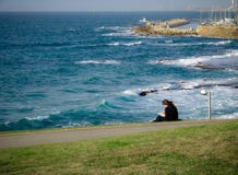Jeune femme s'asseyant sur l'herbe verte au parc, lecture, surveillant une vue de l'océan et du port de Jaffa photos stock Jeune femme s'asseyant sur l'herbe verte au parc, lecture, surveillant une vue de l'océan et du port de Jaffa photos stock