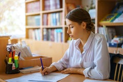 Jeune femme s'asseyant à la table en chemise blanche et journal de signature, concept d'affaires images libres de droits Jeune femme s'asseyant à la table en chemise blanche et journal de signature, concept d'affaires images libres de droits