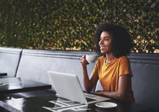 Jeune femme sûre de sourire s'asseyant en café avec l'ordinateur portable sur la table photographie stock libre de droits Jeune femme sûre de sourire s'asseyant en café avec l'ordinateur portable sur la table photographie stock libre de droits