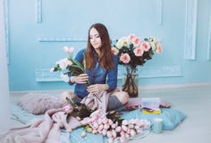 Jeune femme élégante s'asseyant sur le plancher, faisant le bouquet de fleur des tulipes roses dans la pièce ensoleillée légère a image libre de droits Jeune femme élégante s'asseyant sur le plancher, faisant le bouquet de fleur des tulipes roses dans la pièce ensoleillée légère a image libre de droits
