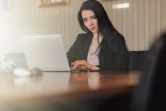 Jeune fille ?motive attirante dans des v?tements de style des affaires se reposant ? un bureau ? un ordinateur portable et ? un t image stock Jeune fille ?motive attirante dans des v?tements de style des affaires se reposant ? un bureau ? un ordinateur portable et ? un t image stock