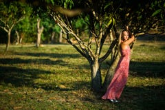 Jeune fille posant dans la robe rose près de l'arbre tropical au coucher du soleil image libre de droits Jeune fille posant dans la robe rose près de l'arbre tropical au coucher du soleil image libre de droits