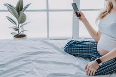 Jeune future mère utilisant le téléphone portable dans sa chambre à coucher photos libres de droits Jeune future mère utilisant le téléphone portable dans sa chambre à coucher photos libres de droits