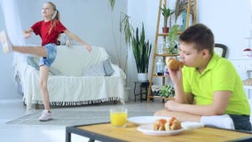 Jeune gar?on mangeant un hot-dog sur le fond d'une fille qui fait des exercices banque de vidéos Jeune gar?on mangeant un hot-dog sur le fond d'une fille qui fait des exercices banque de vidéos