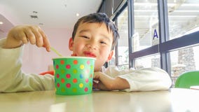 Jeune garçon chinois et caucasien de sourire appréciant mangeant le yogourt glacé Image libre de droits Jeune garçon chinois et caucasien de sourire appréciant mangeant le yogourt glacé Image libre de droits