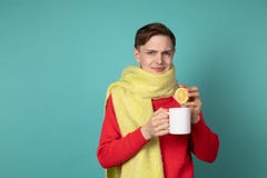 Jeune homme attirant dans le chandail rouge et l'?charpe jaune faisant le visage dr?le, tenant la tasse blanche et le citron coup image stock Jeune homme attirant dans le chandail rouge et l'?charpe jaune faisant le visage dr?le, tenant la tasse blanche et le citron coup image stock